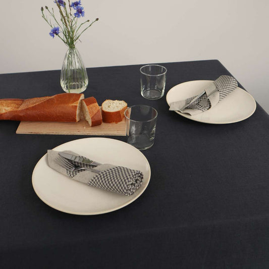Tisch mit dunkelgrauer Tischdecke aus Leinen und Tellern mit Servietten und Besteck